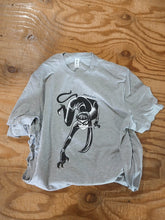 Load image into Gallery viewer, A close-up of the shirt design, featuring a lithe young woman in a catsuit, including tail, crawling toward the camera, printed on it. The woman wears a cat-eye mask and holds a dip pen in her teeth.