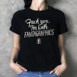 An image of the "Fuck You, I'm With Fantagraphics" design, written in a swirling and blocky font over the Fantagraphics nib logo. The text is printed on a black shirt, pictured on a person standing casually.